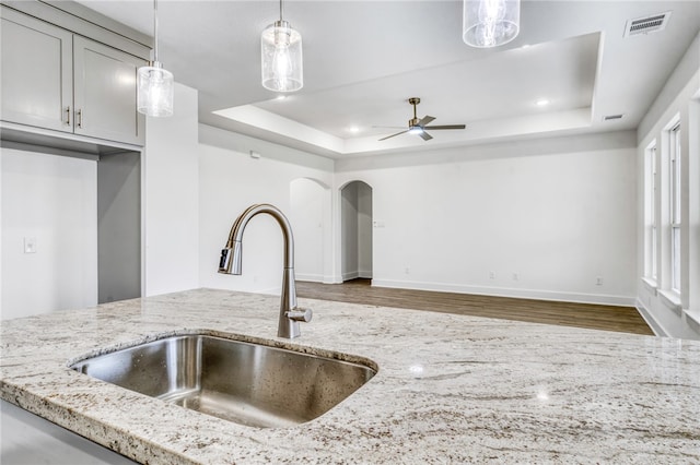 kitchen featuring a tray ceiling, arched walkways, decorative light fixtures, a sink, and light stone countertops