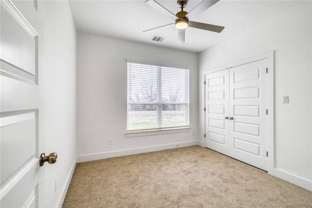 empty room with light carpet, ceiling fan, visible vents, and baseboards