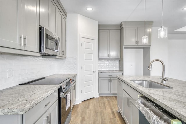 kitchen with light stone counters, light wood-style flooring, stainless steel appliances, a sink, and hanging light fixtures