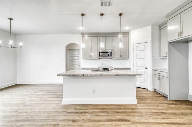 kitchen with stainless steel microwave, a kitchen island with sink, and gray cabinetry