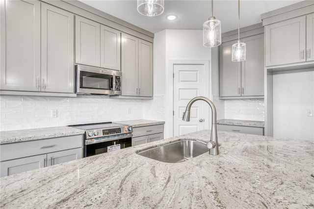 kitchen with light stone counters, stainless steel appliances, gray cabinets, hanging light fixtures, and a sink