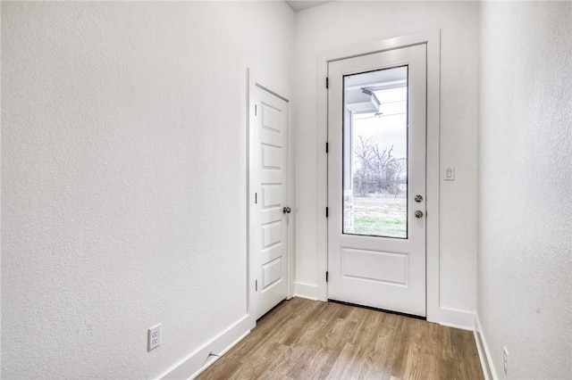 doorway to outside featuring baseboards, a textured wall, and light wood finished floors