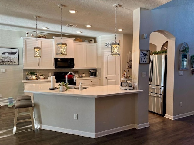 kitchen with black appliances, dark hardwood / wood-style floors, hanging light fixtures, and a kitchen island with sink