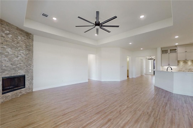 unfurnished living room featuring a raised ceiling, ceiling fan, a fireplace, and light hardwood / wood-style floors