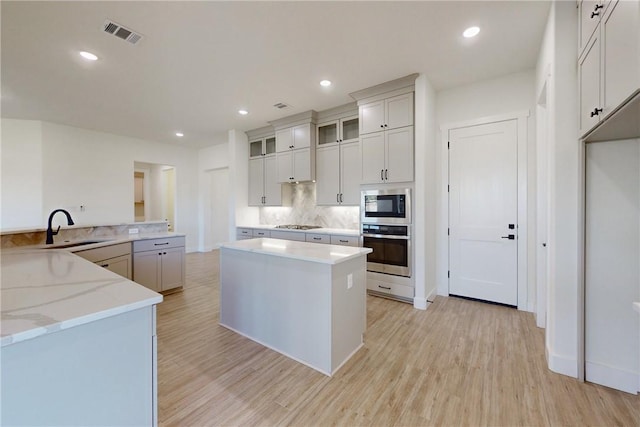 kitchen featuring tasteful backsplash, light stone counters, stainless steel appliances, sink, and light hardwood / wood-style flooring