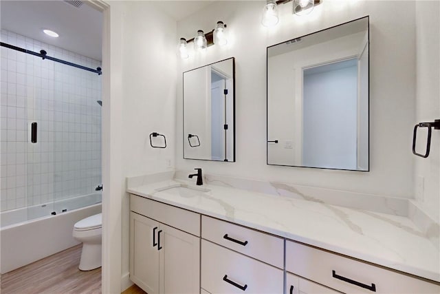 full bathroom with bath / shower combo with glass door, vanity, wood-type flooring, and toilet