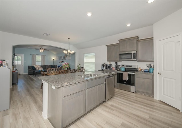 kitchen featuring light stone countertops, light wood-type flooring, appliances with stainless steel finishes, arched walkways, and a sink