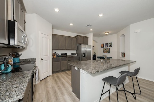 kitchen with a breakfast bar area, light wood-type flooring, dark stone counters, stainless steel appliances, and a sink