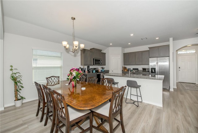 dining area featuring arched walkways, recessed lighting, baseboards, and light wood-style floors