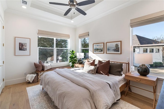 bedroom featuring baseboards, visible vents, a raised ceiling, crown molding, and light wood-style floors