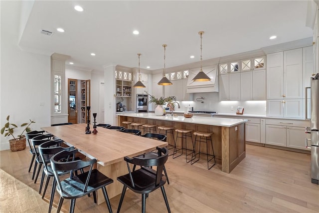 kitchen featuring decorative light fixtures, a spacious island, light countertops, glass insert cabinets, and white cabinets