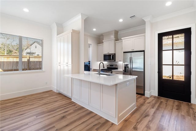 kitchen with white cabinets, appliances with stainless steel finishes, ornamental molding, light countertops, and a sink