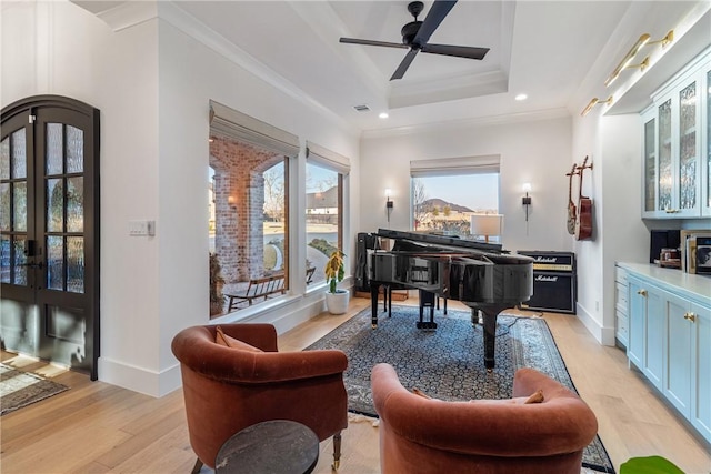 living area featuring a raised ceiling, ornamental molding, heating unit, french doors, and light wood-style floors