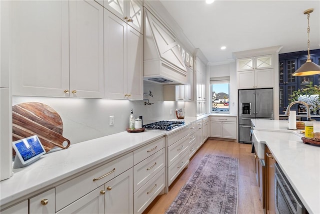 kitchen with premium range hood, white cabinets, appliances with stainless steel finishes, glass insert cabinets, and pendant lighting