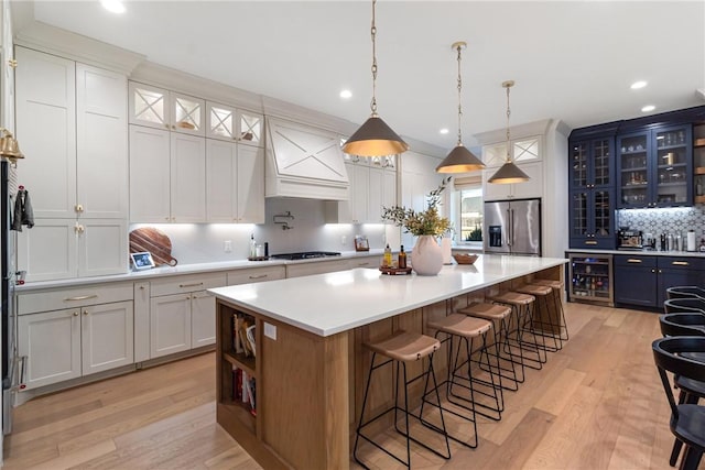 kitchen with beverage cooler, stainless steel appliances, a spacious island, light countertops, and glass insert cabinets