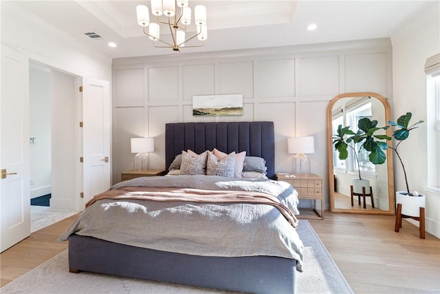 bedroom featuring a tray ceiling, a decorative wall, and light wood-style flooring