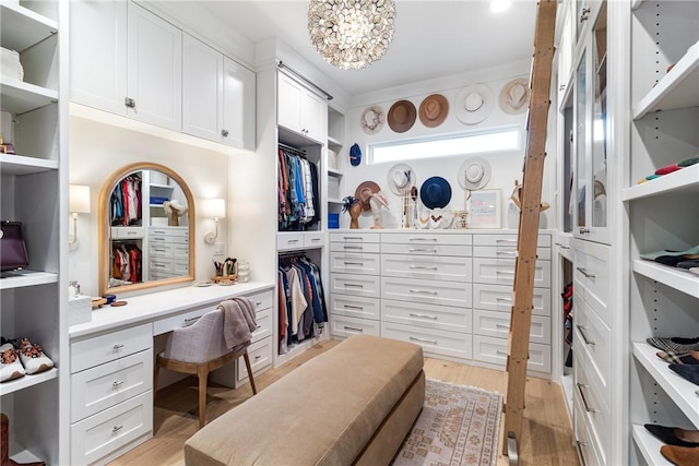 spacious closet with light wood finished floors, a notable chandelier, and built in desk