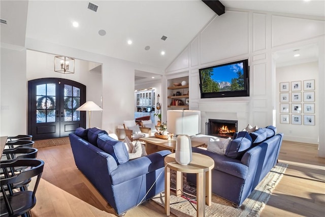 living area with built in shelves, beam ceiling, french doors, light wood finished floors, and visible vents