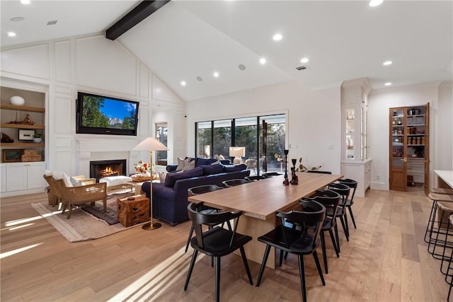 dining area with visible vents, high vaulted ceiling, light wood-type flooring, beamed ceiling, and a lit fireplace