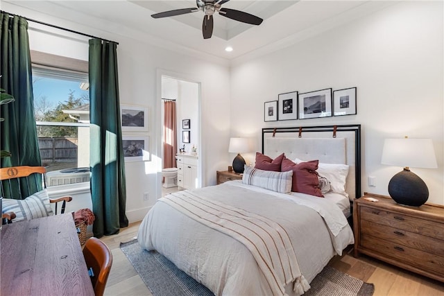 bedroom with ensuite bath, light wood-style flooring, ceiling fan, and a raised ceiling