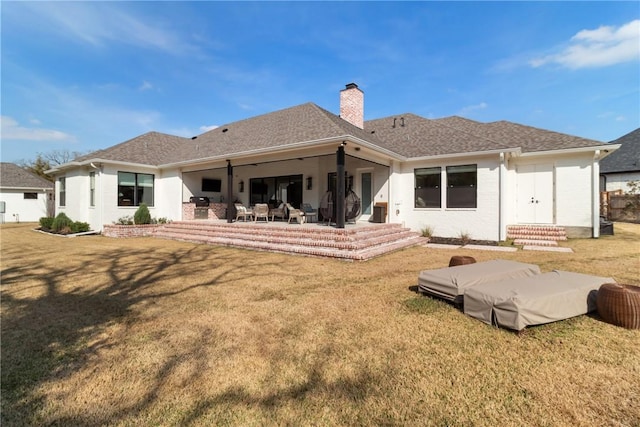 back of property with a shingled roof, a yard, a chimney, and a patio