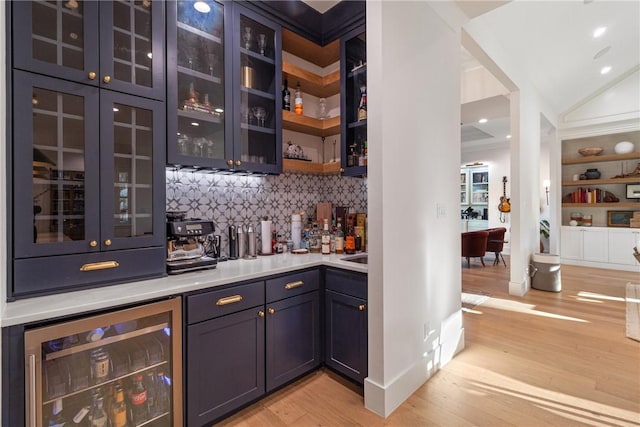 bar with a dry bar, tasteful backsplash, light wood-style floors, vaulted ceiling, and beverage cooler