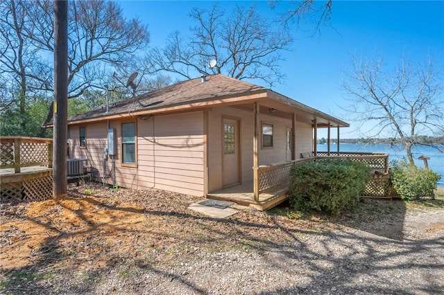 view of property exterior featuring a water view, covered porch, a shingled roof, and central AC