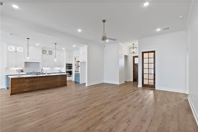 kitchen with a spacious island, white cabinetry, hanging light fixtures, and light wood-type flooring