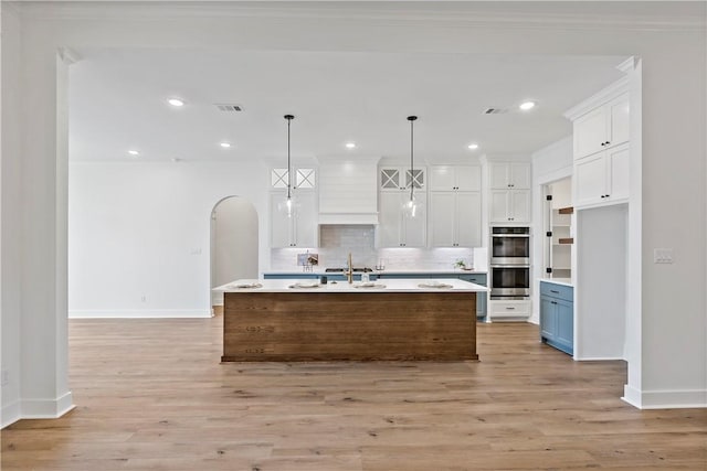 kitchen featuring white cabinetry, double oven, decorative light fixtures, and a center island with sink