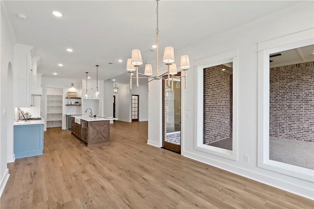 kitchen featuring white cabinetry, an island with sink, sink, hanging light fixtures, and light wood-type flooring