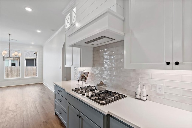 kitchen with pendant lighting, ornamental molding, decorative backsplash, custom exhaust hood, and stainless steel gas stovetop