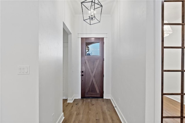 doorway featuring ornamental molding, a notable chandelier, and light hardwood / wood-style flooring