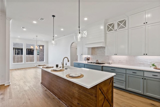 kitchen with sink, white cabinetry, decorative light fixtures, an island with sink, and backsplash