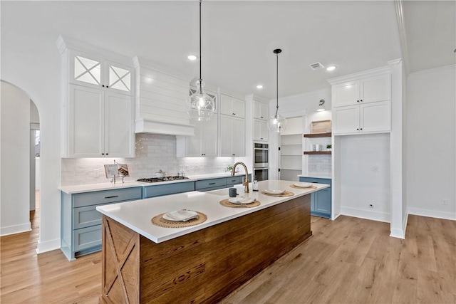 kitchen featuring appliances with stainless steel finishes, white cabinetry, sink, hanging light fixtures, and a center island with sink