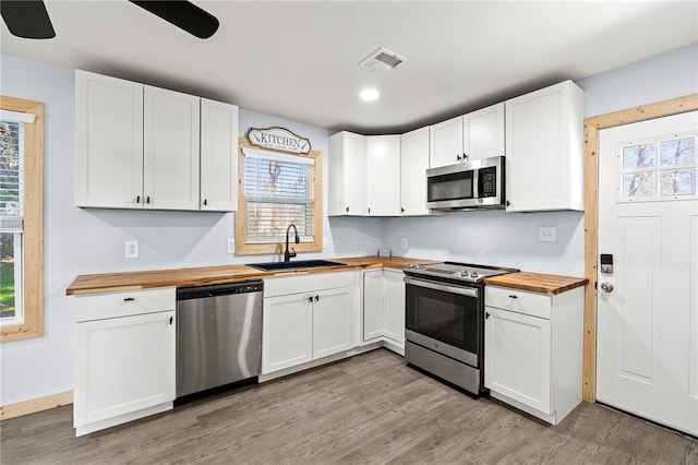 kitchen with butcher block countertops, sink, white cabinets, and stainless steel appliances