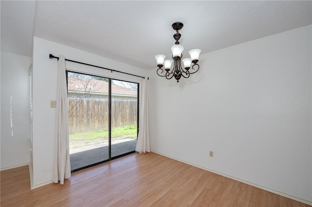 spare room with light wood-style floors, a notable chandelier, and baseboards