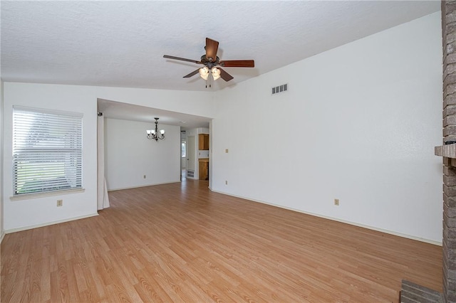 unfurnished living room with light wood-style flooring, ceiling fan with notable chandelier, visible vents, vaulted ceiling, and a brick fireplace