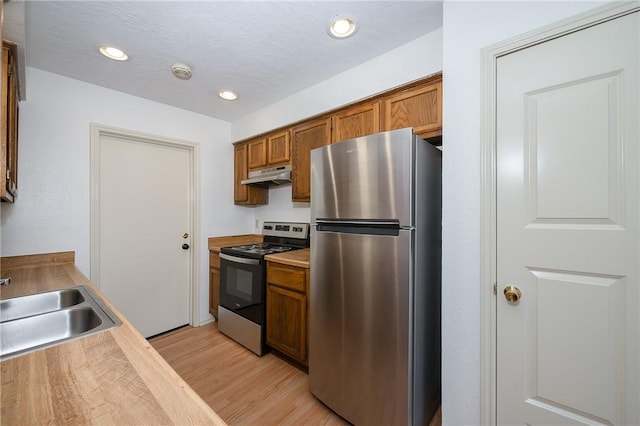 kitchen with brown cabinets, stainless steel appliances, light countertops, under cabinet range hood, and a sink