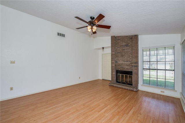 unfurnished living room featuring a textured ceiling, visible vents, a ceiling fan, a brick fireplace, and light wood finished floors