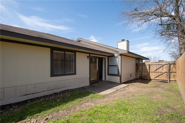 back of property featuring a gate, a chimney, fence, and a lawn