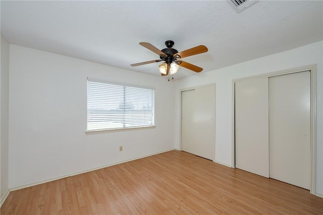 unfurnished bedroom featuring light wood finished floors, ceiling fan, visible vents, and multiple closets