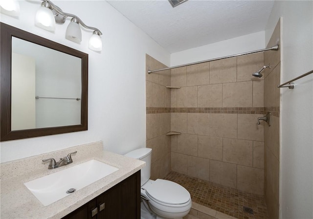 bathroom with toilet, a textured ceiling, tiled shower, and vanity