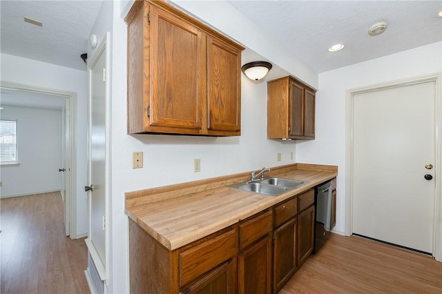 kitchen featuring light wood-style floors, brown cabinetry, a sink, and dishwasher