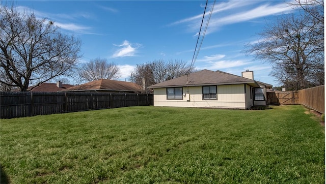 rear view of property featuring a yard, a chimney, and a fenced backyard