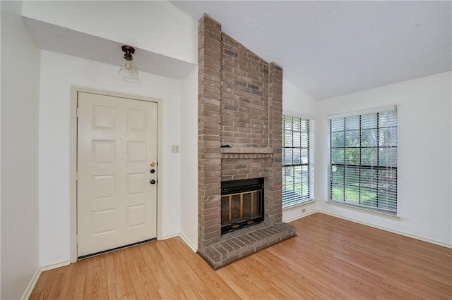 foyer entrance featuring a brick fireplace, vaulted ceiling, light wood-style flooring, and baseboards