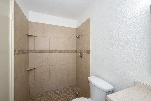 bathroom featuring a textured wall, tiled shower, and toilet