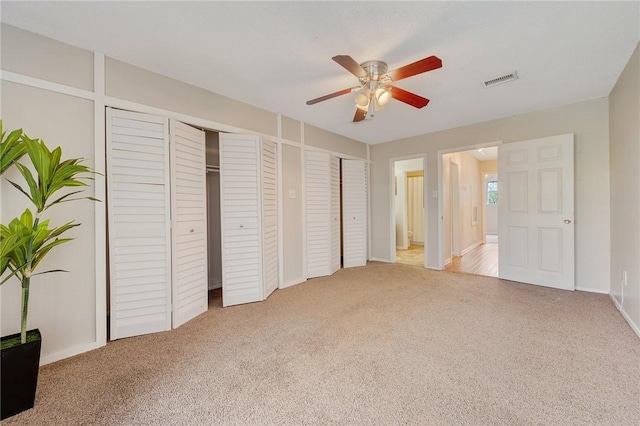 unfurnished bedroom featuring light carpet, two closets, and ceiling fan