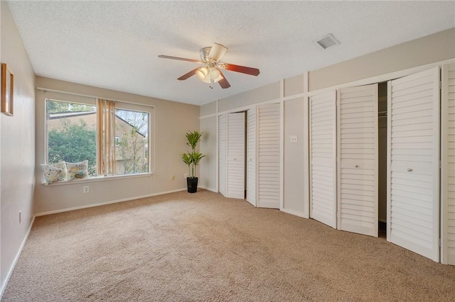 unfurnished bedroom featuring carpet flooring, multiple closets, ceiling fan, and a textured ceiling