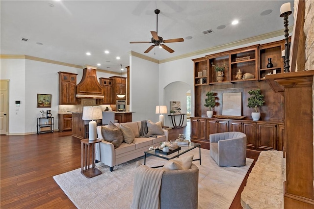 living area with arched walkways, crown molding, a ceiling fan, dark wood-type flooring, and recessed lighting