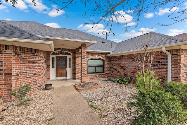 view of exterior entry featuring brick siding and a shingled roof